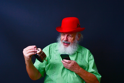 An old American gentleman in a red bowler hat and green guayabera shirt comparing the time on a smartphone and alarm clock