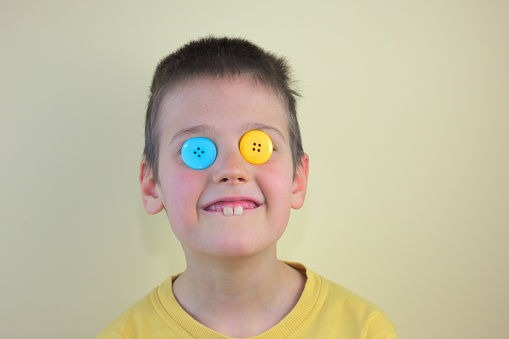 A cute funny caucasian kid carrying blue and yellow buttons on his eyes