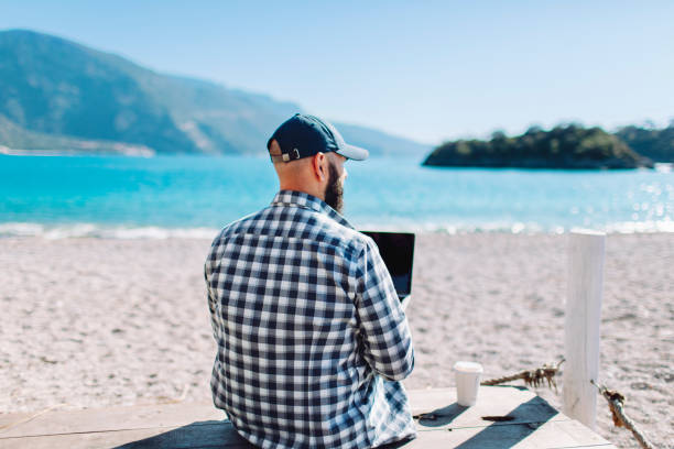 istock Young adult man working at the beach using laptop 1464968362