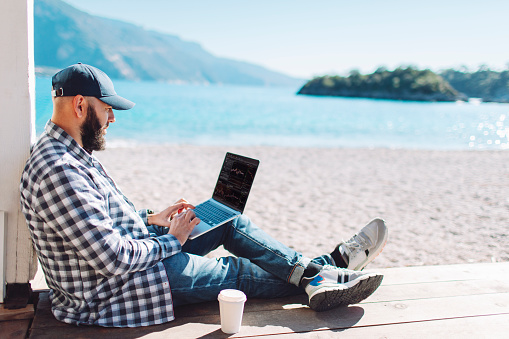 Young adult man working at the beach using laptop
