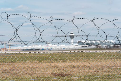 Security fence at the airport. In the background are blurred runway and other airport buildings like tower and terminal. Airport security concept