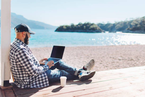 istock Young adult man working at the beach using laptop 1464969365