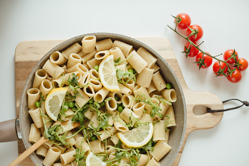 A shot of a pan of rigatoni pasta with lemons, greens, and cherry tomato decoration ready for serving.