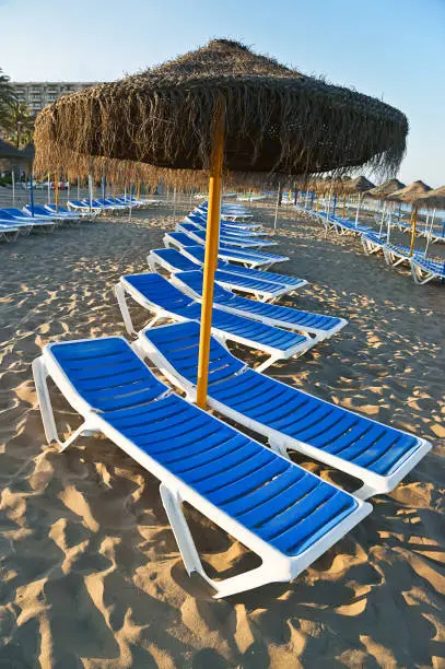 Photo of Vertical shot of a straw umbrella and  sun loungers on a beach in Torremolinos, Malaga, Spain