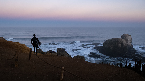 surfer walking to go surfing, sunrise at punta de lobos, Pichilemu, Chile. View to iconic natural place Los Morros