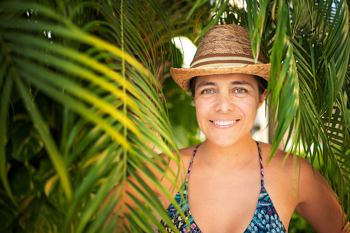 An attractive female in a swimsuit and hat under a palm tree