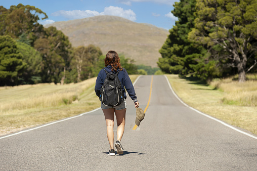 A middle-aged Argentinian woman holding her cap and walking on the mountain road