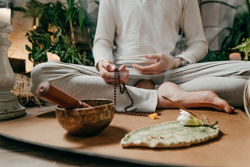Close-up of man holding rosary in his hands meditating sitting on cork mat with singing bowl and aroma stick. Meditation and harmony.