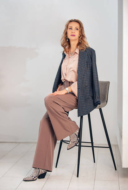 Women's business clothes in pink pastel colors. Palazzo trousers with a wide belt, silk blouse, jacket and snakeskin cowboy boots.. Powdery pink color. A harmonious combination of shades of color in clothing. checkered cowboy boots stock pictures, royalty-free photos & images