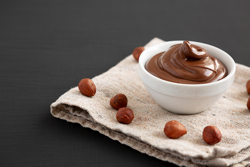 Homemade Chocolate Hazelnut Spread in a Bowl on a black background, side view. Copy space.