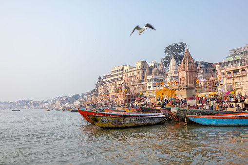 Varanasi, Uttar Pradesh, India - November 2022: Historic Varanasi city with ancient temples and buildings architecture along the anges river ghat as viewed from a boat during sunrise.