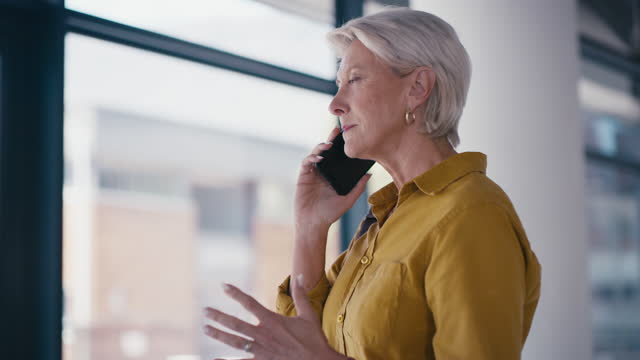 Phone call, senior and woman at a window in office building for negotiation, proposal and networking.  Elderly, lady and entrepreneur in online discussion for advice, idea and thinking while planning