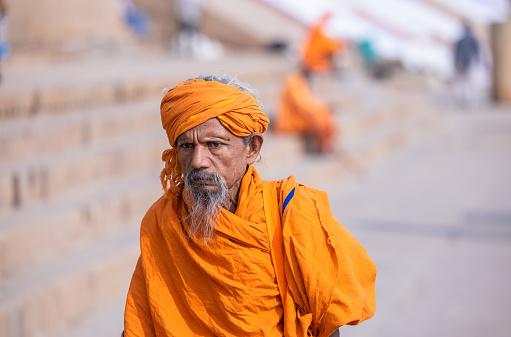 Varanasi, Uttar Pradesh, India - November 2022: Portrait of Unidentified Indian sadhu holy man in traditional saffron clothes on ghats near river ganges in varanasi city.
