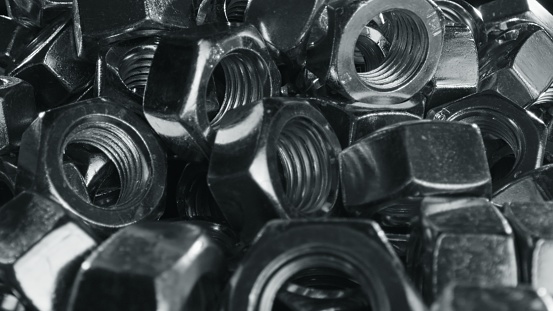 Huge pile of silver nuts fasteners scattered on black tabel - close up