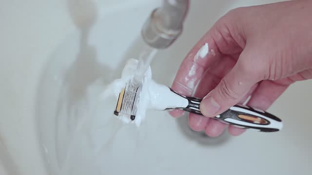 The man rinses his razor with tap water.
