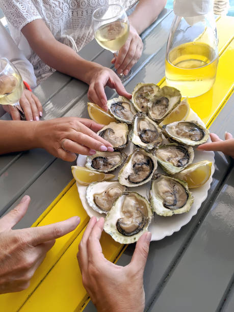 A group of friends are tasting oysters and white wine in a restaurant on the sea coast, a concept for a gastronomic tour stock photo