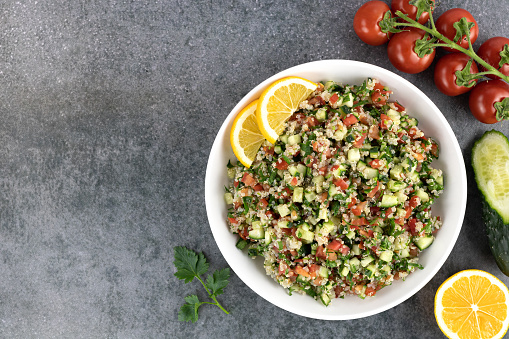 Levantine Tabouleh salad with quinoa, cucumbers, tomatoes, parsley on a gray background. Top view. Copy space. Middle Eastern or Arabic cuisine.