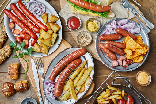 Tasty and colorful barbecue for social gathering, breakfast, brunch or lunch, protein meal, sausages and baked potato with cheese bread, sliced cucumber Spanish onion, parsley, mustard and ketchup sauce, served on a metal plates, on a wooden home, bar or restaurant table, a close up image with a copy space, top view image