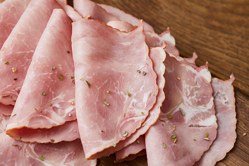 View of an elegant arrangement on a black slab of cooked ham or prociuto cotto with a head of garlic on a rustic wooden board.