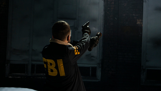 FBI agent with a gun aiming in a darkness on a street, we see him from the back. FBI unifom