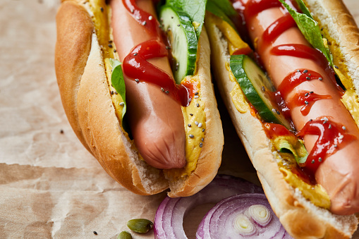 Two tasty hotdogs served on a recyclable paper, on a wooden home, bar or restaurant table, a close up image with a copy space