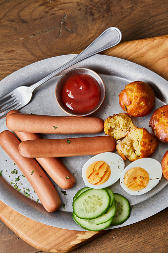 Tasty hotdogs with cheese bread and eggs, ketchup sauce and fresh organic cucumber, served on a metal plate, on wooden home, bar or restaurant table, a close up image with a copy space, top view image