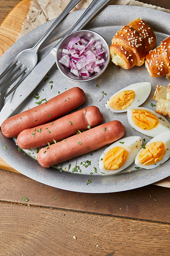 Healthy protein breakfast, hotdog sausages and eggs, old cheese with truffles and fresh organic Spanish onion, served on a metal plate, on wooden home, bar or restaurant table, a close up image with a copy space, top view image