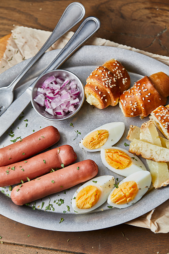 Healthy protein breakfast, hotdog sausages and eggs, old cheese with truffles and fresh organic Spanish onion, served on a metal plate, on wooden home, bar or restaurant table, a close up image with a copy space, top view image