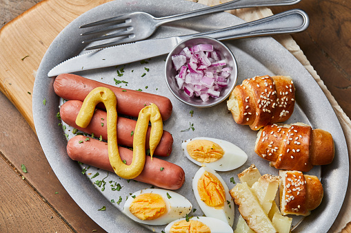 Healthy protein breakfast, hotdog sausages and eggs, old cheese with truffles and fresh organic Spanish onion, served on a metal plate, on wooden home, bar or restaurant table, a close up image with a copy space, top view image