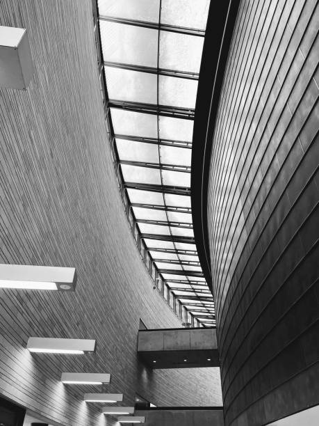 istock Black and white monochrome modern building interior curved narrow corridor hall with ceiling windows and lamps on the wall 1465026045