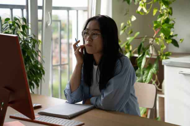 istock Focused Asian female student studying at home attending virtual class, taking online course 1465028399