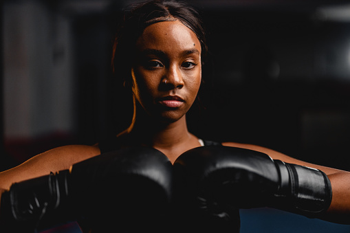 Headshot of a confident young Hispanic female boxer wearing boxing gloves and sports clothes. She is looking at the camera.