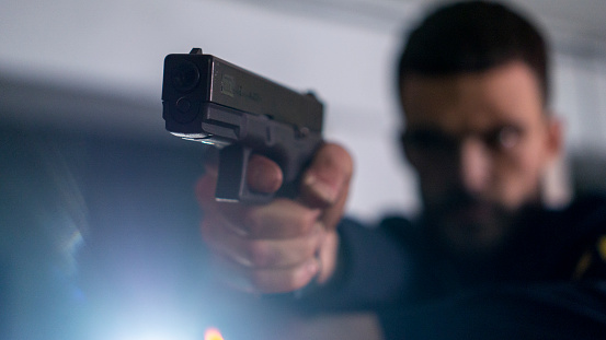 Close-up of a muzzle of a gun in the hands of a bearded gloomy man in a dark jacket
