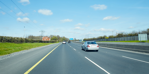 Rear view of cars driving on motorway, Ireland. Road with metal safety barrier or rail. cars on the asphalt under the cloudy blue sky. Highway traffic.