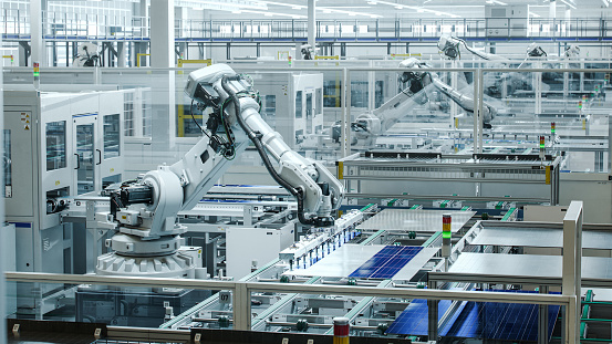 White Industrial Robot Arm at Production Line at Modern Bright Factory. Solar Panels are being Assembled on Conveyor. Automated Manufacturing Facility