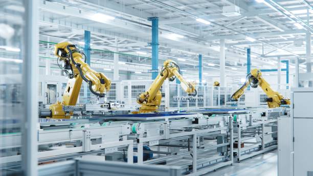 large production line with industrial robot arms at modern bright factory. solar panels are being assembled on conveyor. automated manufacturing facility - indústria imagens e fotografias de stock