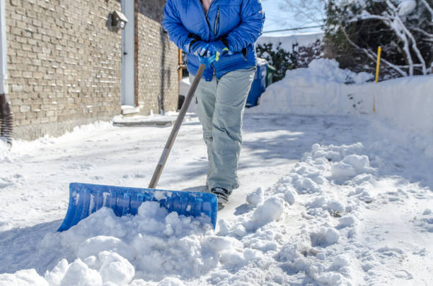 Close up on shovel pushing snow by woman in car driveway after a snowstorm
