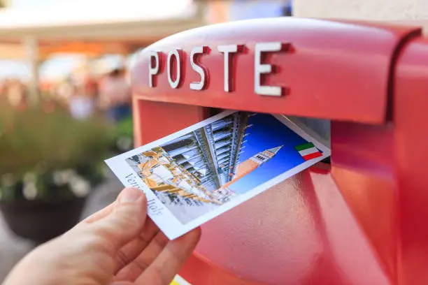 Photo of Man drop a postcard to a vintage mailbox in Venice, Italy. The postcard shows a San Marco square.