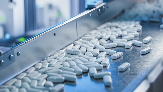 White Pills are Moving on Conveyor at Modern Pharmaceutical Factory. Tablet and Capsule Manufacturing Process. Close-up Shot of Medical Drug Production Line.