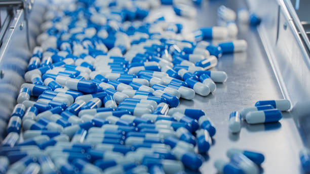 istock Tablet and Capsule Manufacturing Process. Capsules are Moving on Conveyor at Modern Pharmaceutical Factory. Close-up Shot of Medical Drug Production Line. 1465073102