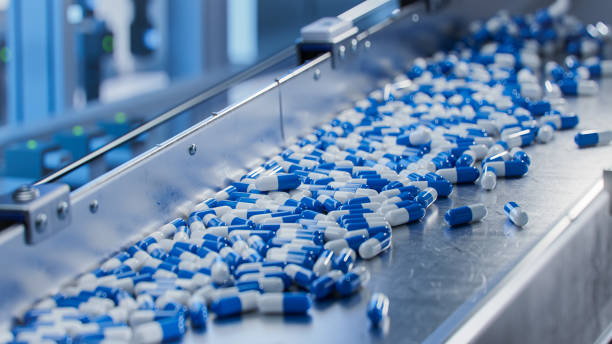 cápsulas azules en transportador en fábrica farmacéutica moderna. proceso de fabricación de tabletas y cápsulas. primer plano de la línea de producción de medicamentos médicos. - capsule pill medicine antibiotic fotografías e imágenes de stock