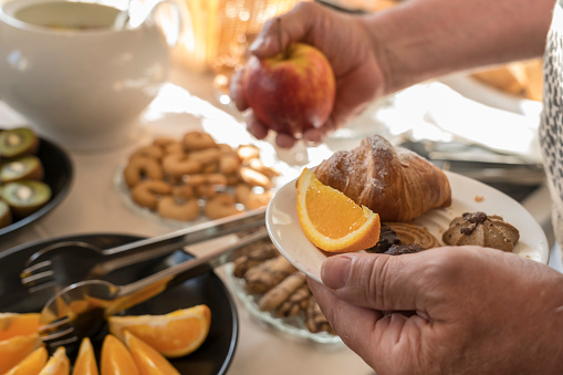 Male hand reaching for an apple at self-service breakfast at the hotel. On the table is fruit, croissant and biscuits.