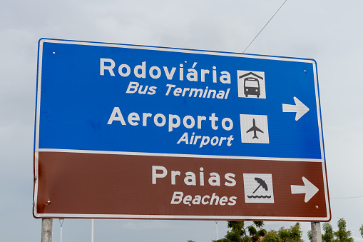 Direction sign with indications to the bus terminal, airport and beaches, with texts in Portuguese and English.