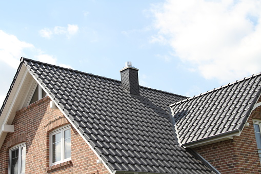 Residential house rooftop, ventilated peak and red brick chimney covered with a metal grate and wire mesh screen to prevent wildlife from entering the chimney.