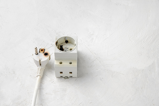 An example of a short circuit in the network. Burnt plug and socket close-up, gray concrete background, copy space. electrical safety