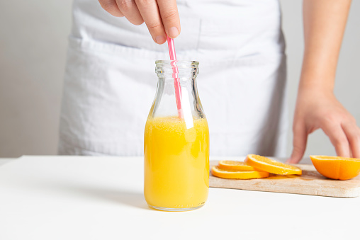 Unrecognizable caucasian female is squeezing orange juice into a drinking glass on a white table.