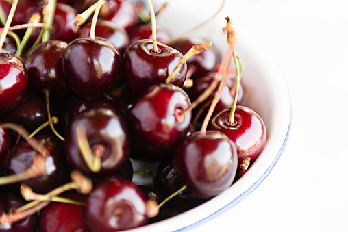 Fresh cherries in a black bowl on a white isolated  background. Top view and copy space.