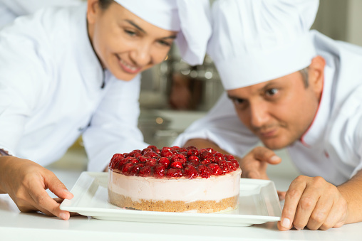 One female chef  and one male chef are looking at cheesecake with raspberry in commercial kitchen.