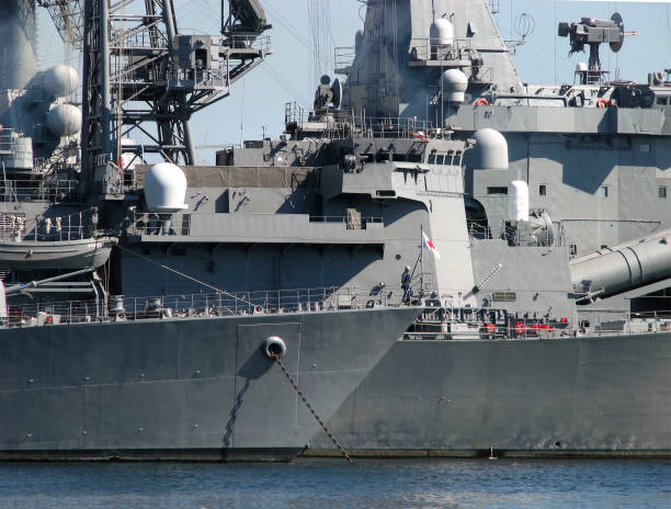 A modern warship is anchored in port with a European city in the background (Stockholm)