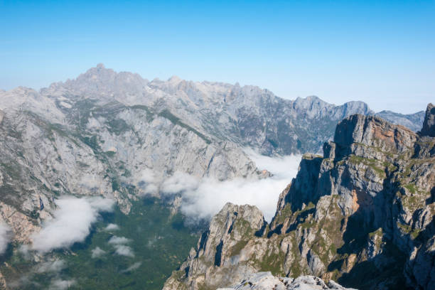 Scenic view of majestic rocky mountains rise above white clouds with a vibrant blue sky in the background. Picos de Europa, nature reserve in Spain